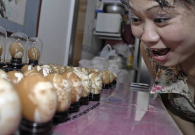 A Chinese woman shows intersts in the eggs carved with the portraits of famous soccer players at the home Chinese artist Wang Huaping in Tianjin, China, 9 July 2010 clipart