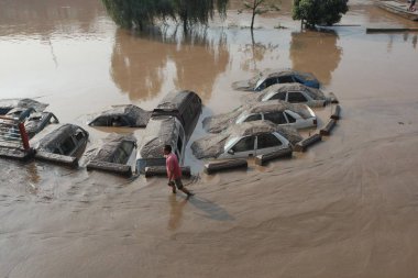A Chinese man walks past cars submerged by floodwaters in Chongqing, China, July 21, 2010 clipart