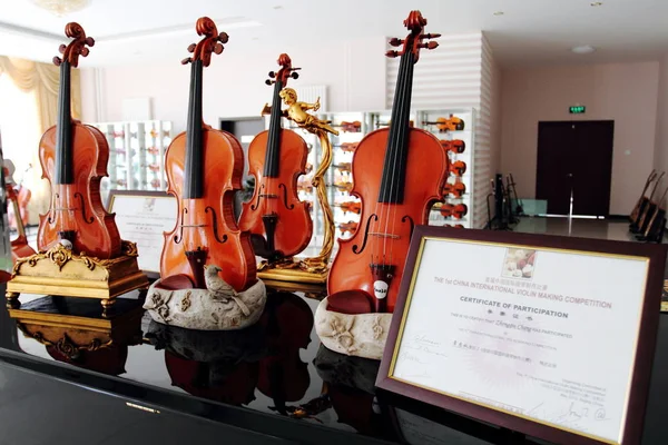 ヴァイオリンは 2010年8月12日 北京市東国町にある北京華東楽器株式会社の工場のショールームで ヴァイオリン作りの表彰状の横に展示されています — ストック写真