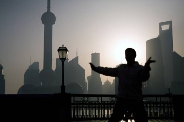 A man practises Tai-chi (Taiji, Tai Chi, shadow-boxing) on the Bund in the early morning, as the landscape of the Pudong  Lujiazui Financial District is seen in the background, Shanghai, China, March 14, 2009. clipart