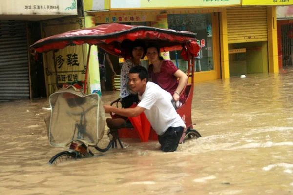 中国人男性は 2009年8月9日 日曜日 中国浙江省東部のレチン市で起こった台風モラコットによる豪雨の後 2人の女性と三輪車を押しのけます — ストック写真