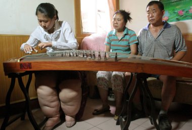 Wang Cheng, left, 23, who suffers from Lymphedema, which caused fat legs, plays Guzheng, a traditional Chinese zither with 21 strings, and her parents look on at home in Xuzhou, east Chinas Jiangsu province 12 June 2007 clipart
