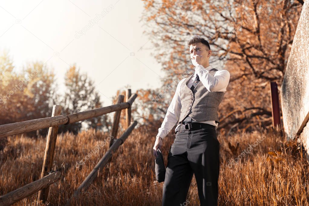 Classic young man smoking in a natural park at sunset