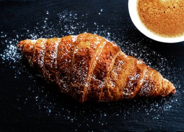 Kahvaltıda taze pişmiş kruvasan içeren bir fincan kahve