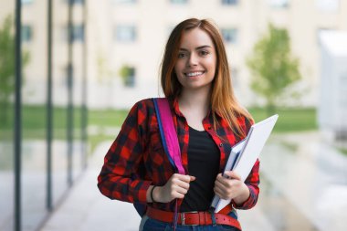 Sırt çantası ve elinde kitapla gülümseyen bir kızın portresi.