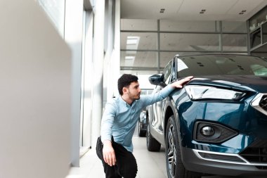 Adam bir galeride yeni arabasına el ele tutuşuyor.