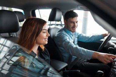 Yeni arabalarının içinde bir araba galerisinde oturan neşeli genç çift.