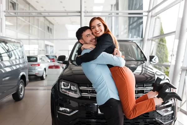 Guy hugs his girlfriend in a car dealership on the background of a purchased car