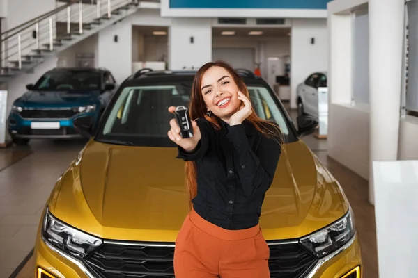 Joyful pretty young woman with a key in hands near her new car