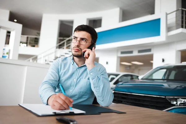 Pensive car dealership employee talking on the phone and writing