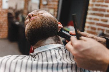 Berber ustası sakalını elektrikli budama makinesiyle kesiyor.