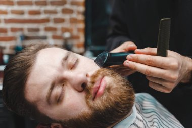 Usta kuaför, müşterinin sakalını elektrikli makasla keser.