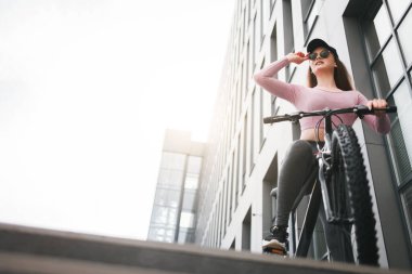 Bisikletli şık bir kız düz görünüyor. Şapkalı kadın ve açık havada bisiklet süren gözlüklü kadın.