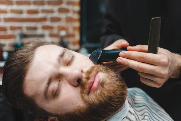 Master hairdresser cuts client\'s beard with electric trimmer