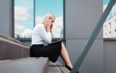 Yorgun ofis çalışanı merdivenlerde dizüstü bilgisayarın arkasında kafasını tutarak oturuyor. Fazla çalışma kavramı