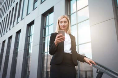 Ofis binasının yakınında elinde telefonla zarif bir iş kadını.