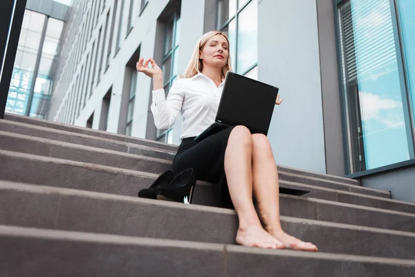 オフィスワーカーは ノートパソコンを備えたオフィスビルの階段に座って瞑想しています 働き過ぎの概念 — ストック写真