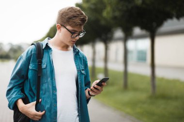 Genç yakışıklı öğrenci internete erişmek için akıllı telefon kullanıyor. Gadget bağımlılığı kavramı