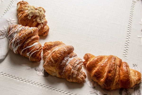 Freshly croissants with almonds,  powdered sugar on a table with napkins and tablecloth, closeup, top view — Stock Photo, Image