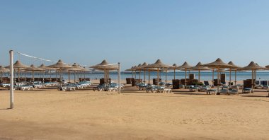 şezlonglar, şemsiyeler ve denize bakan bir voleybol ağı ile terk edilmiş plaj