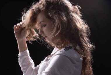 koyu bir duvara karşı şık uzun kıvırcık saçlı genç bir kız profili