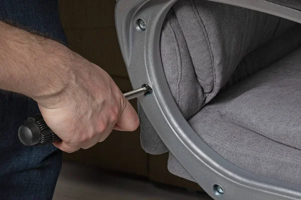 Adam bir sandalyeyi tamir ediyor. Erkeklerin elinde bir tornavida. Montaj ve onarım kavramı