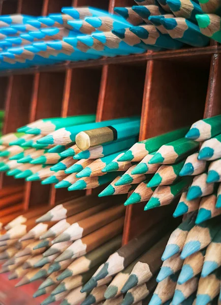 green pencils on shelf in store against the background of pencils of different colors. Pencil background. Inverted pencil on shelf in group with other pencils.