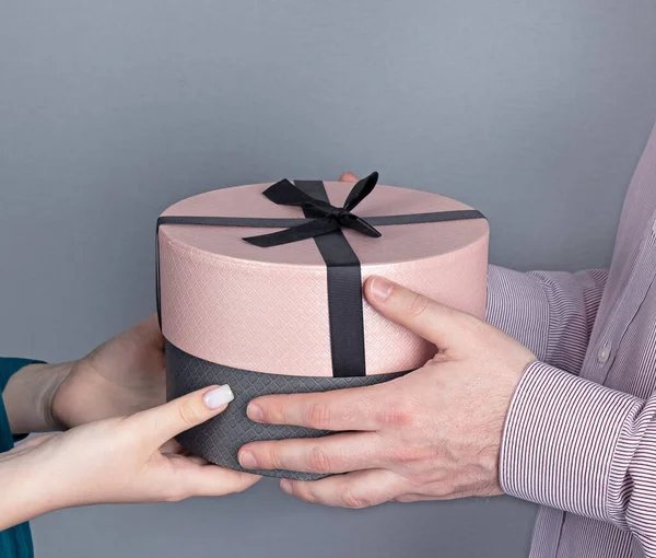 man gives gift to girl. Round box with gift in hands of couple close-up.