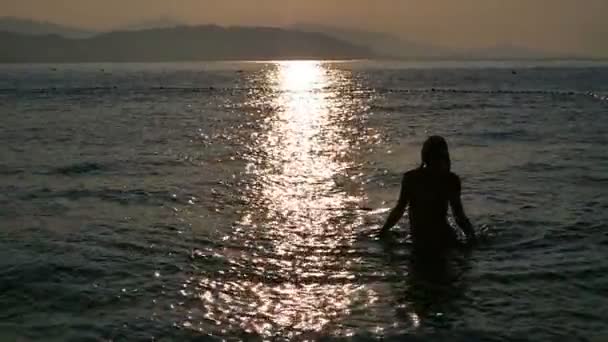 Piękna dziewczyna w czarnym kostiumie kąpielowym pochodzi z morza o świcie. — Wideo stockowe