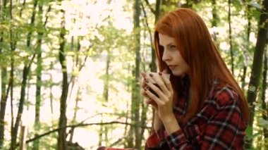 Bir parkta veya ormanda genç kadın bir bardak kahve veya çay içme.