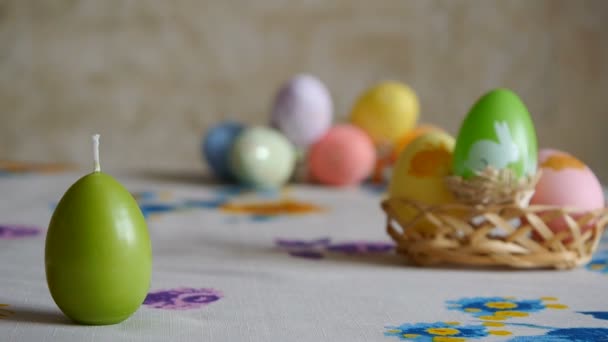 Ženská ruka položila na stůl tři velikonoční svíčky. Zelený, oranžový a žlutý. Barevná velikonoční vajíčka na pozadí. — Stock video