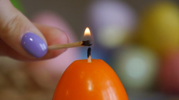Свічки, зроблені у формі великоднього яйця. Помаранчеві свічки. Жіноча рука запалює свічки . — стокове відео