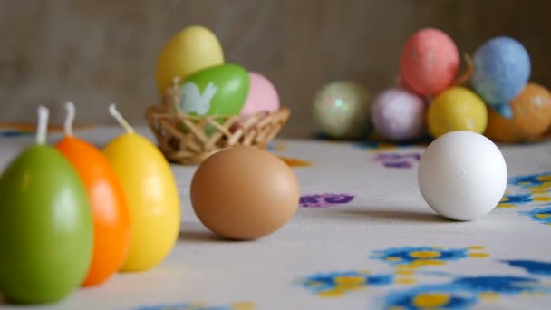 Veselé velikonoce. ženské ruce Sunu stůl dvě velikonoční vajíčka. barvité svíčky a barvité velikonoční vajíčka na pozadí. — Stock video