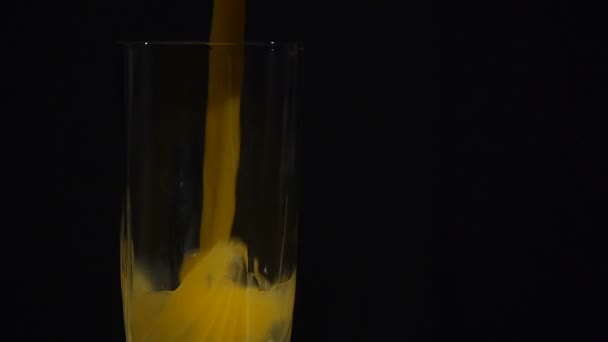 Gros plan. Le jus d’orange est versé dans un grand verre sur un fond noir. Jus d’orange ou d’ananas. — Video