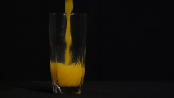 Oranje sap wordt gegoten in een hoog glas op een zwarte achtergrond. Close-up. Biologisch drankje. Sinaasappel of ananas SAP. — Stockvideo