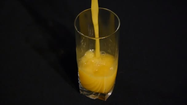 Le jus d’orange ou d’ananas est versé dans un grand verre sur un fond noir. Gros plan. Boisson bio. — Video