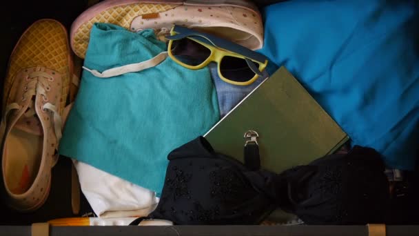 Woman hands are packing suitcase for a journey. Top view. Girl dreams about travel. Goggles for swimming, summer clothes, sneakers, dress. Girl gets ready for flight to resort. Concept of travel. — Stock Video