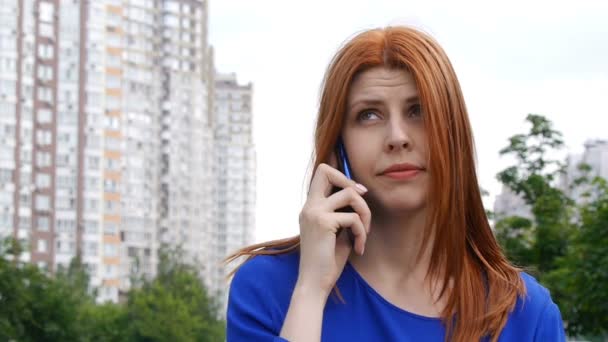 Menina bonita nova com cabelo vermelho está falando seriamente em um telefone celular . — Vídeo de Stock