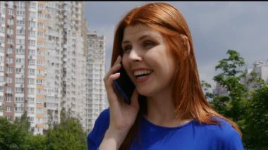 Kızıl saçlı, cep telefonuyla konuşan ve gülümseyen güzel bir kız. Şehirde çok mutluyum..