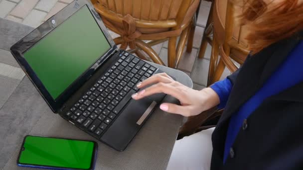 Freelancer woman working with a laptop and mobile phone with green screen in a coffee shop. Close up view. — Stock Video