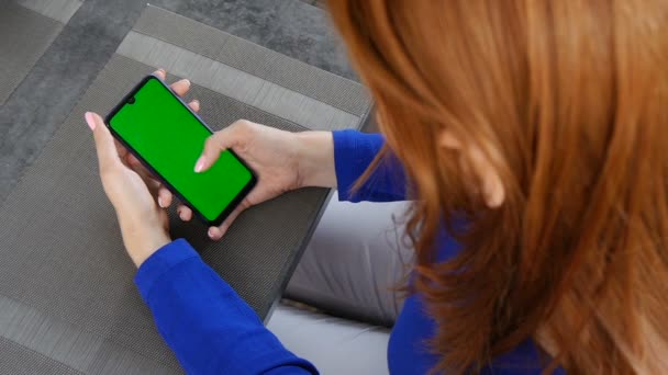 Chica de pelo rojo sentada en la cafetería. Uso de teléfono móvil con pantalla verde. De cerca. . — Vídeos de Stock