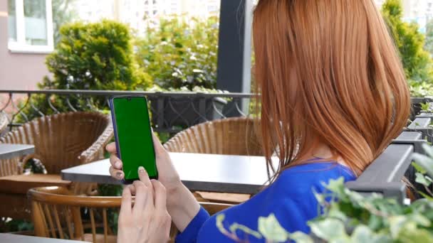 女孩红头发坐在舒适的咖啡馆。使用带绿屏的手机. — 图库视频影像
