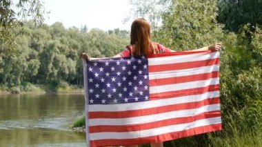 Kız genç kadın genç kadın bir Amerikan Usa Stars and Stripes bayrağı nı kapaya salar. Nehrin yanında durmak.