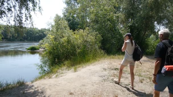 Homme et fille, père et fille, marchez ensemble. Voyageurs avec sacs à dos. Ils s'arrêtent sur la rive de la rivière et regardent dehors . — Video