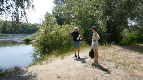 男人和女孩一起徒步旅行。带背包的徒步旅行者。他们停在河岸上，看着它. — 图库视频影像