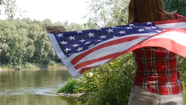 Jeune femme adolescente tenant un drapeau américain des USA Stars and Stripes. Debout près de la rivière . — Video