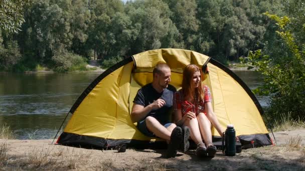 Junges glückliches Paar kommt ins Zelt und entspannt sich. Mädchen küsst einen Kerl. Sie haben einen romantischen Moment. Wald und Fluss im Hintergrund. — Stockvideo