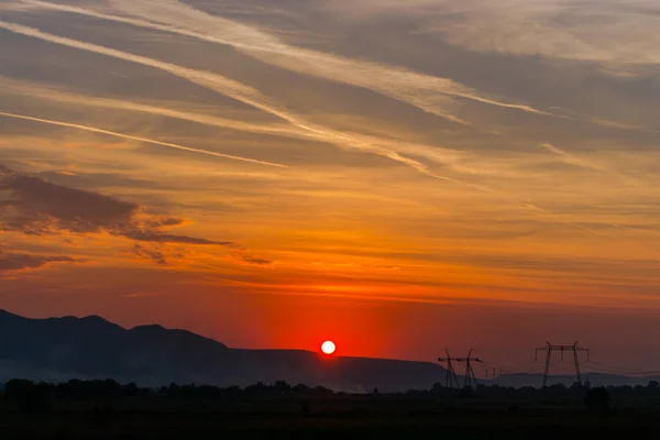 landscape with setting sun in cloudy sky over distant mountains