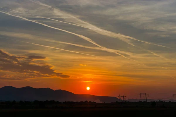 landscape with setting sun in cloudy sky over distant mountains