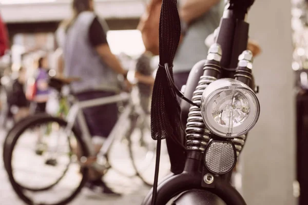 Vintage bicycle, detail of the front light, in classic cycling convention. Participants behind, out of focus.